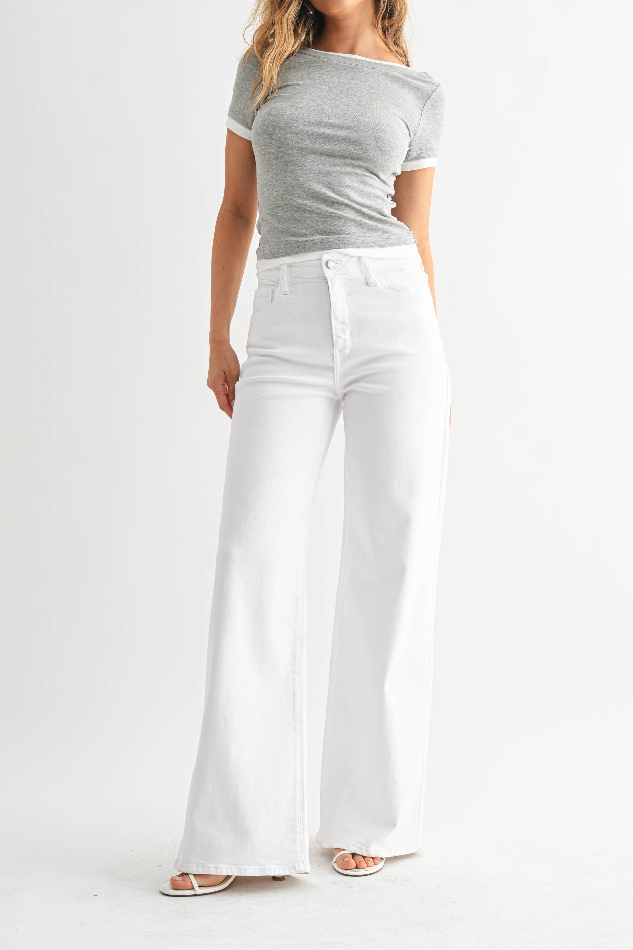 Woman wearing a gray off-shoulder top and white wide-leg pants on a white background