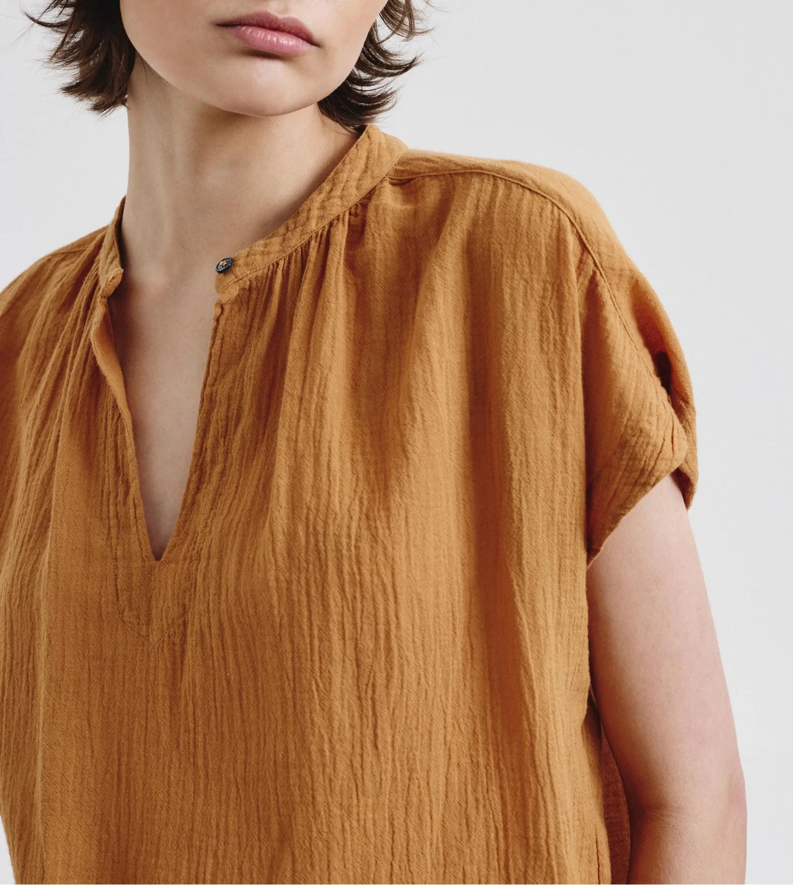 Woman wearing a mustard yellow blouse against a plain background