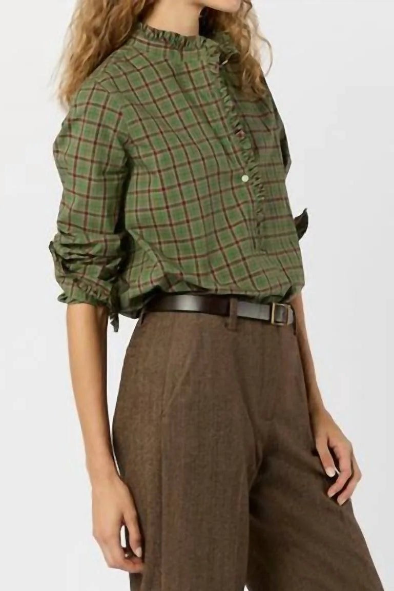 Person wearing a green plaid shirt and brown pants on a white background