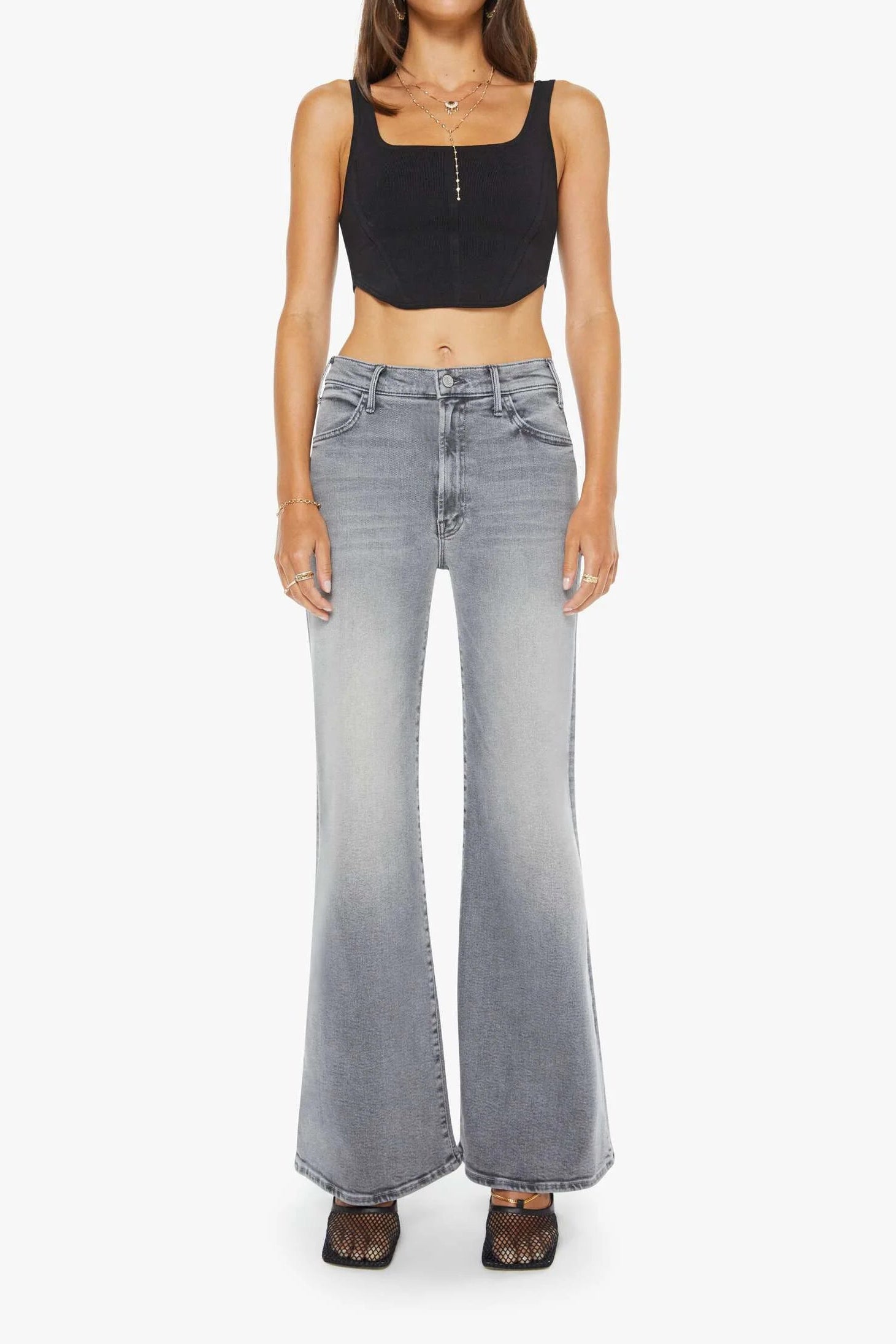 Woman wearing a black tank top and gray flared jeans on a white background