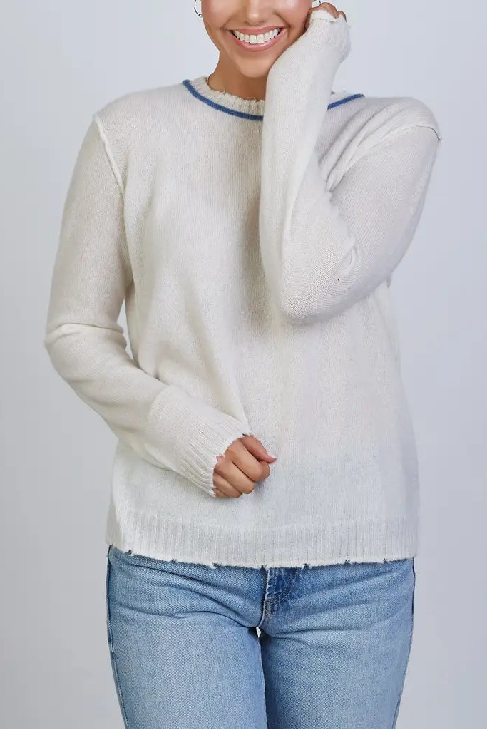 Woman wearing a light gray sweater and blue jeans against a plain background