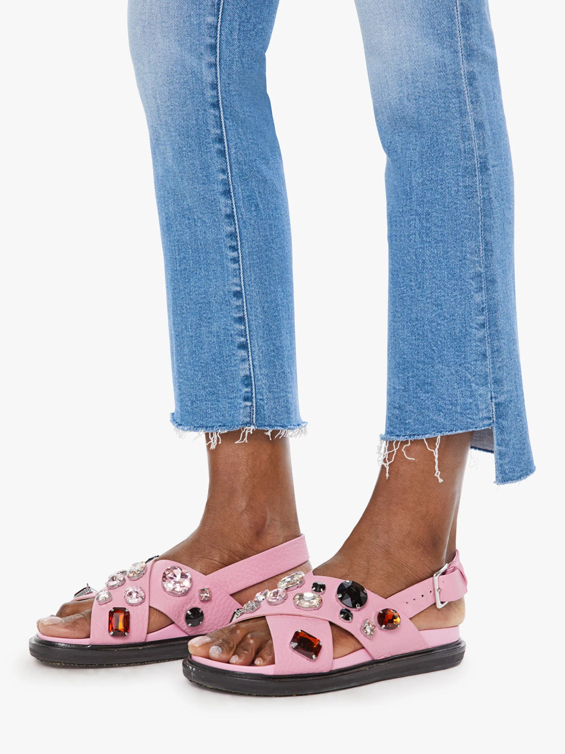 Pink sandals with gemstones worn with blue jeans on a white background