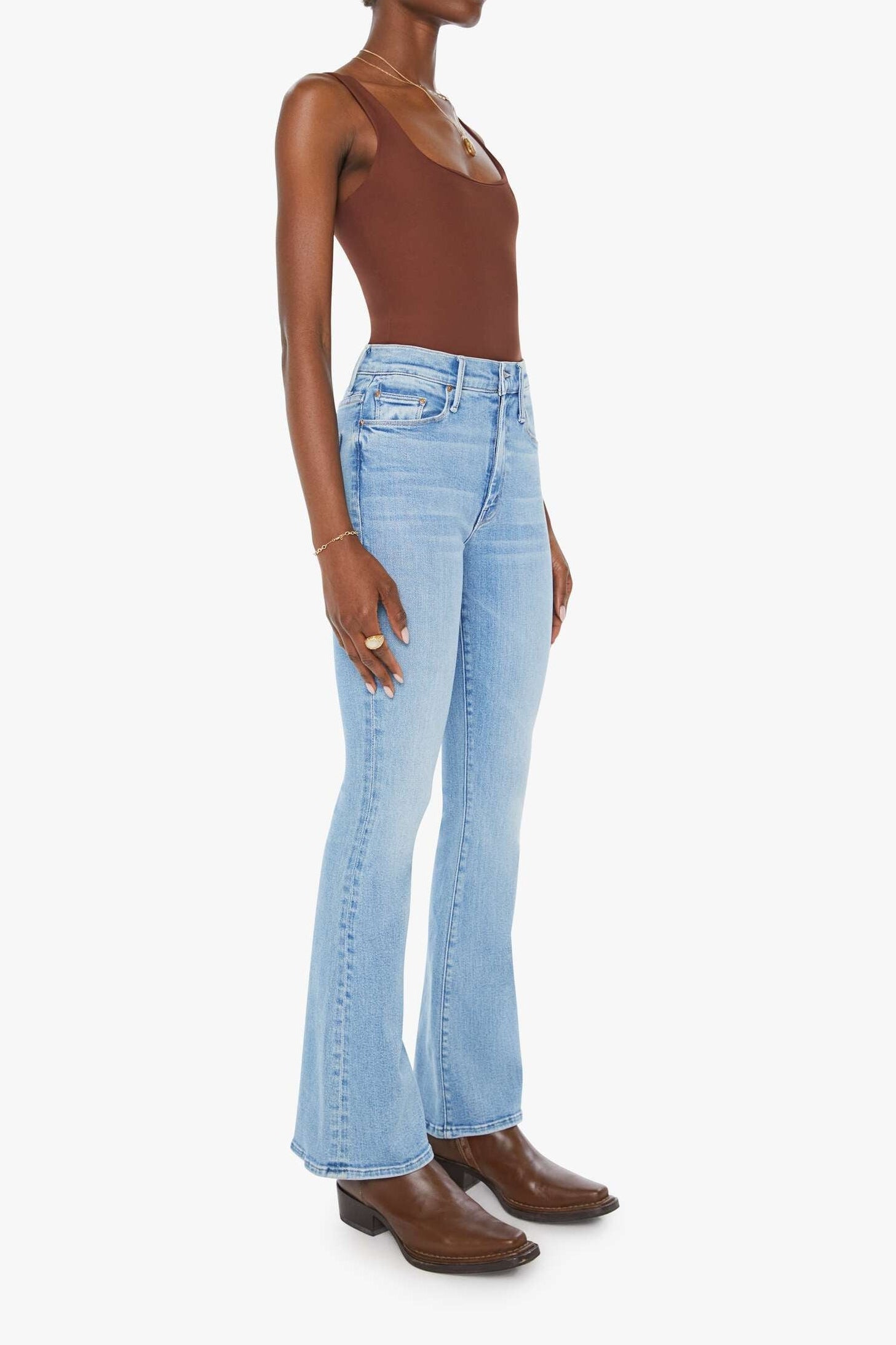 Woman wearing light blue flared jeans and brown boots on a white background