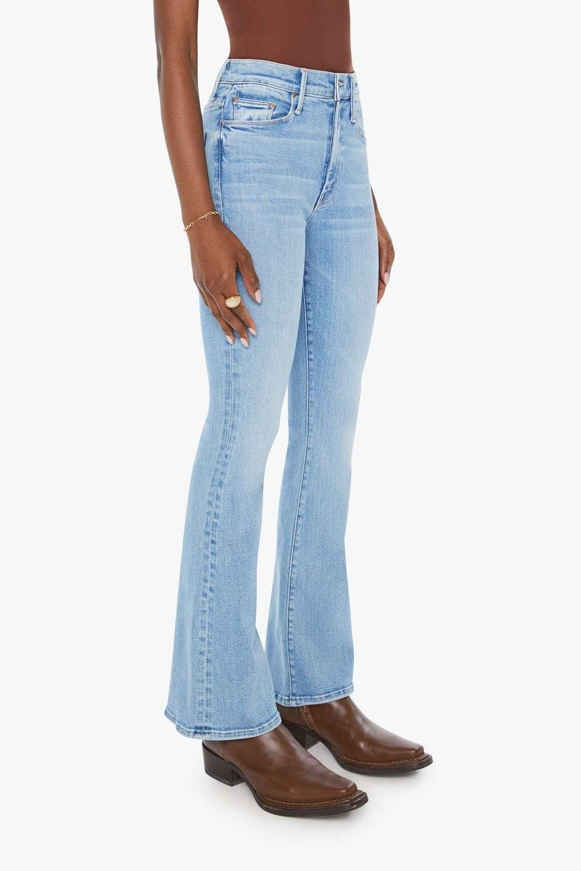 Woman wearing light blue flared jeans and brown boots on a white background