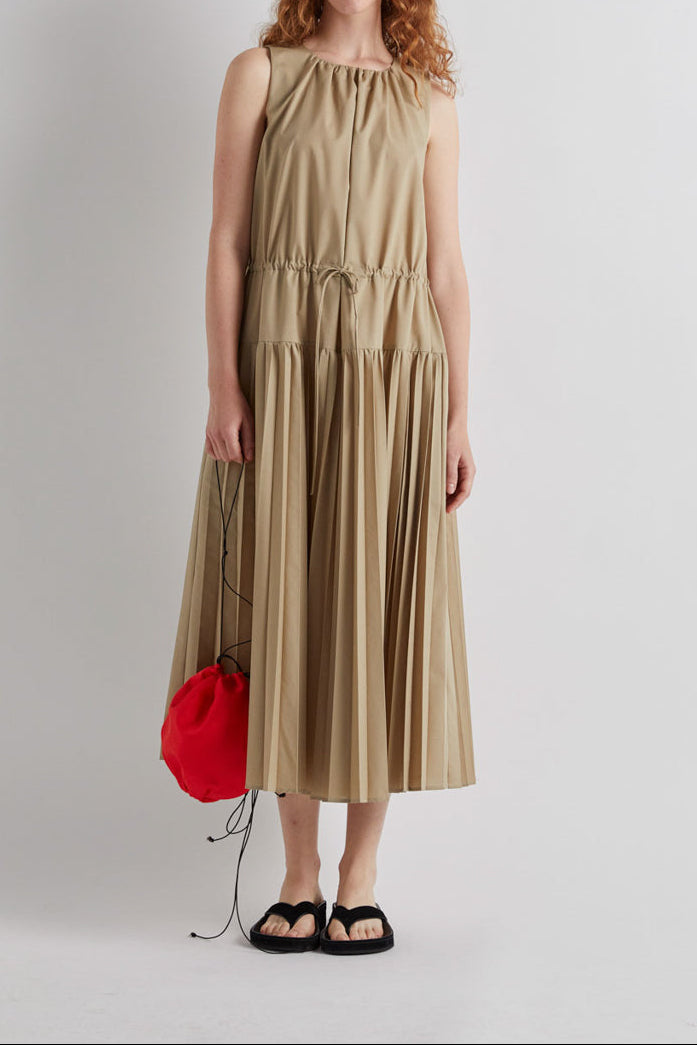 Woman wearing a beige dress with a red bag on a white background