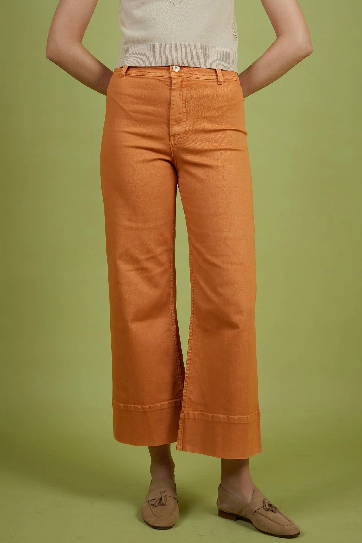 Person wearing orange pants and a light-colored top on a green background
