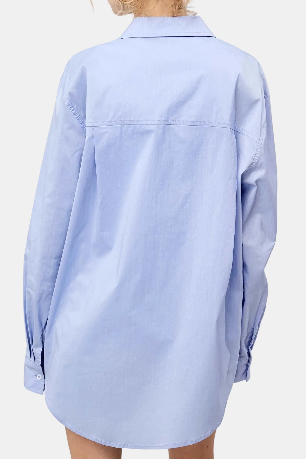 A light blue long-sleeve button-up shirt shown from the back on a model, featuring a relaxed oversized fit and a collar.