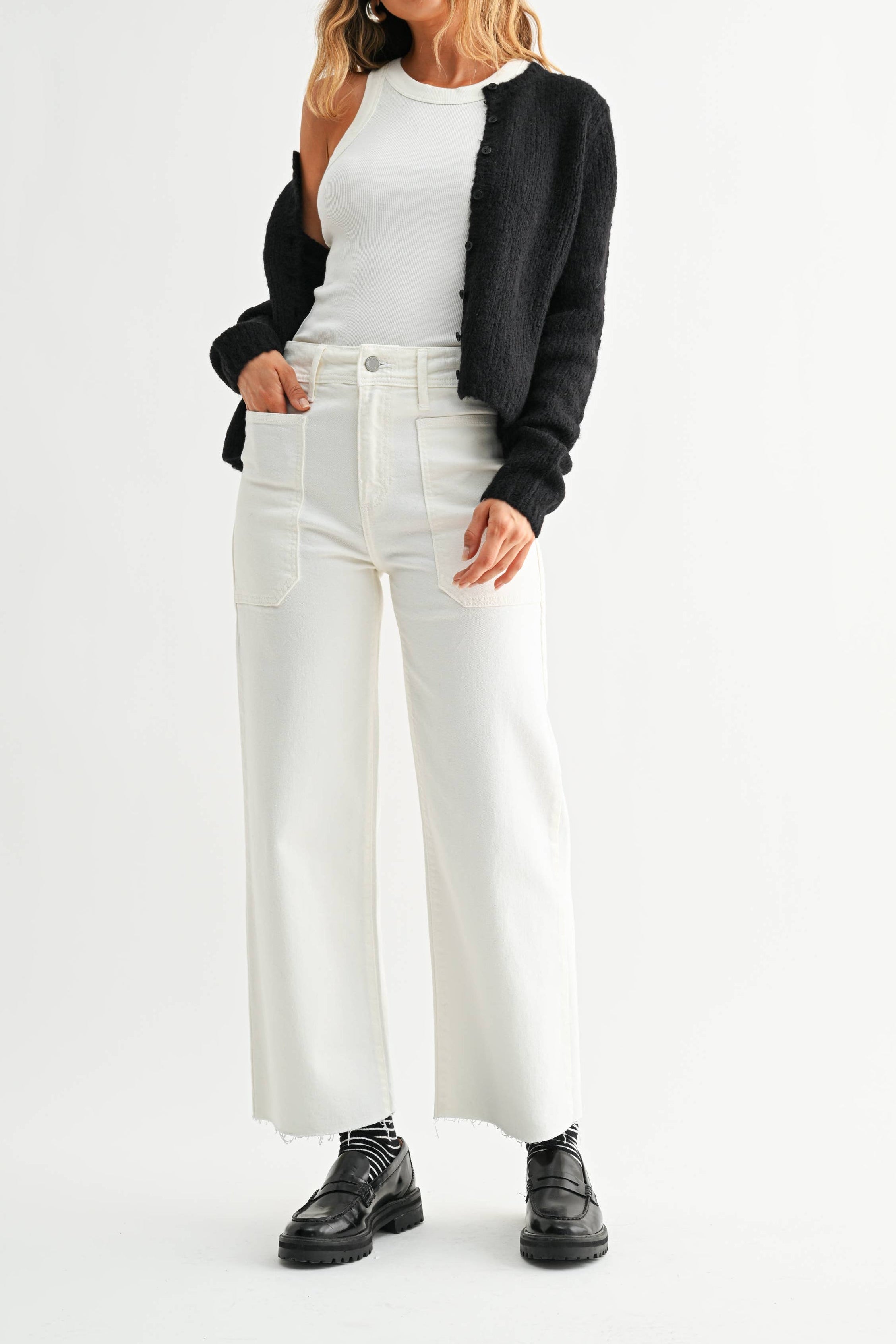 Woman wearing a black cardigan, white top, and white pants on a white background