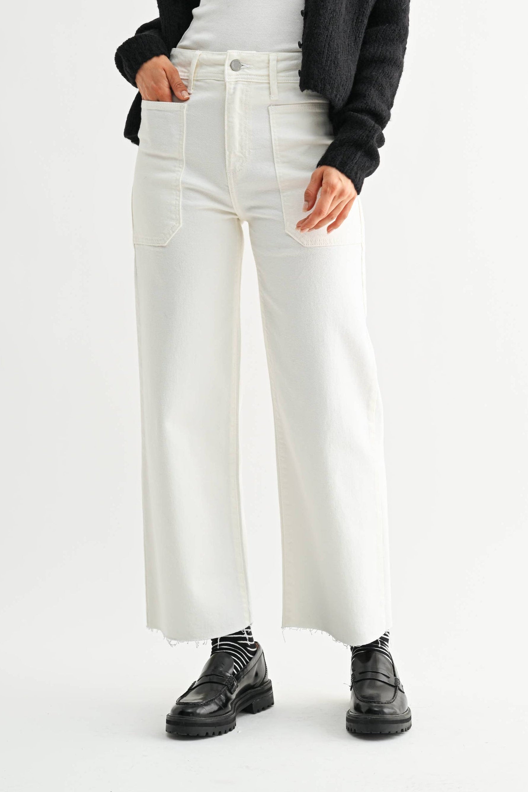 Woman wearing a black cardigan, white top, and white pants on a white background