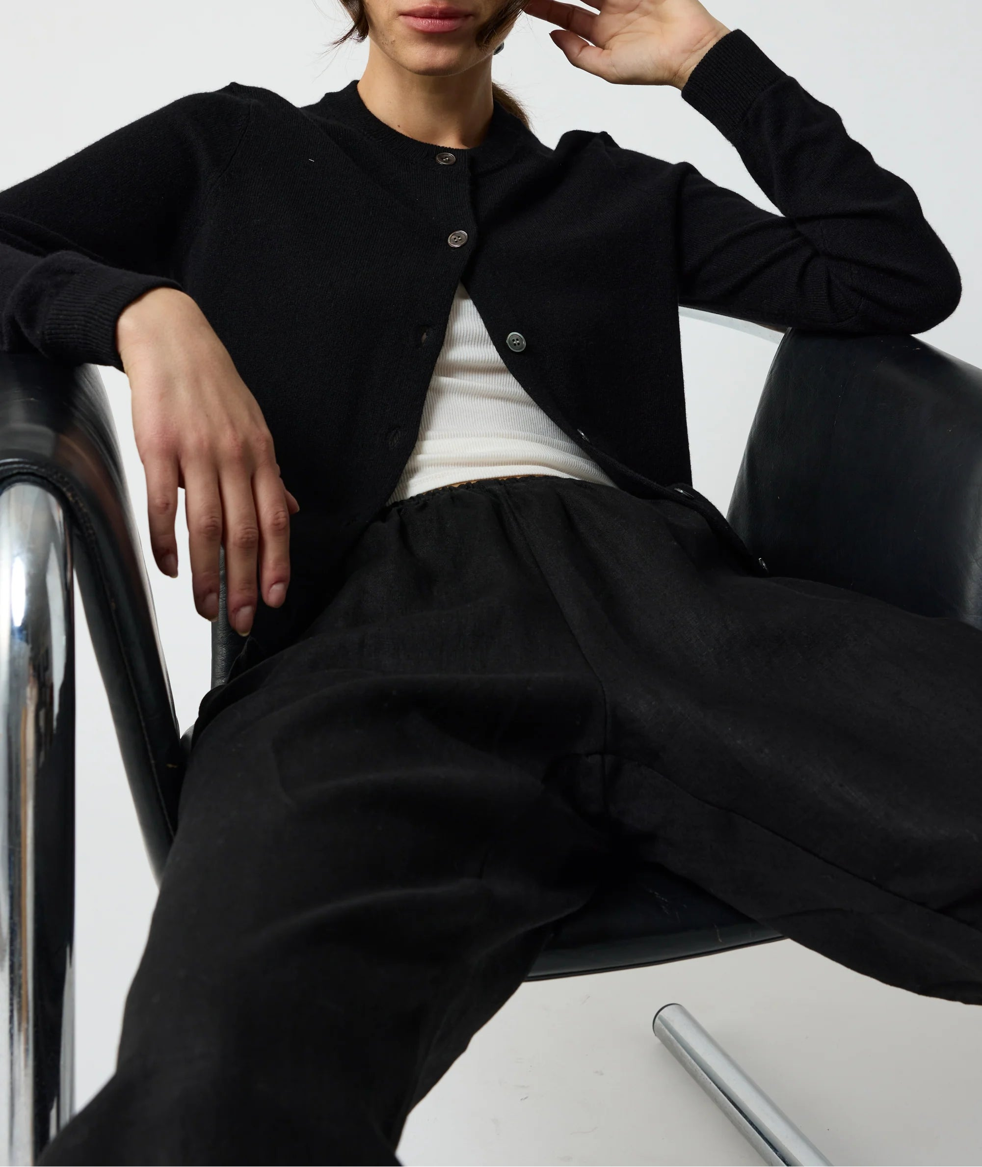 Person wearing a black jacket and pants sitting on a chair against a white background