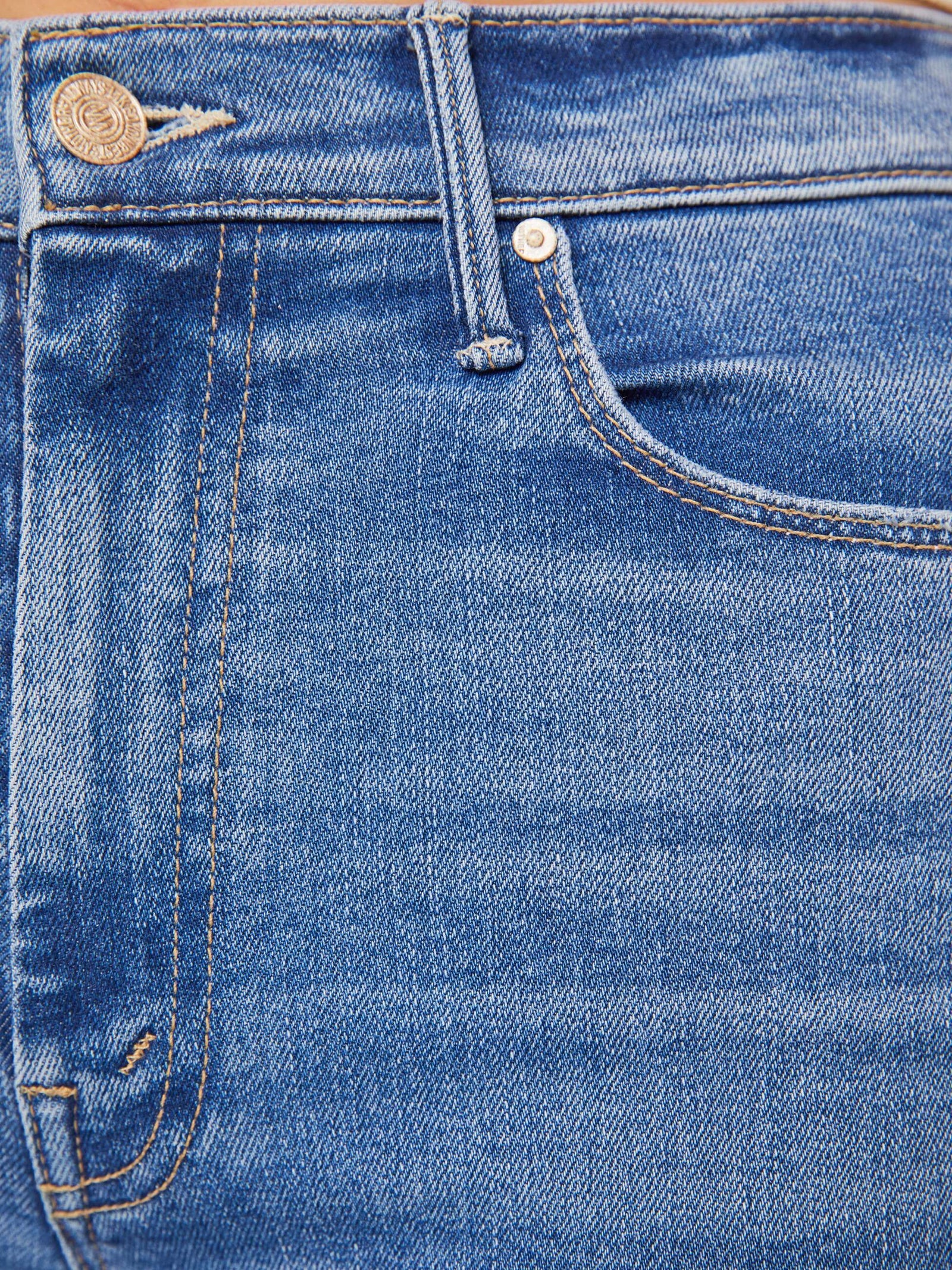 Close-up of blue denim jeans showing the waistband, belt loop, button, front pocket, and contrast stitching.