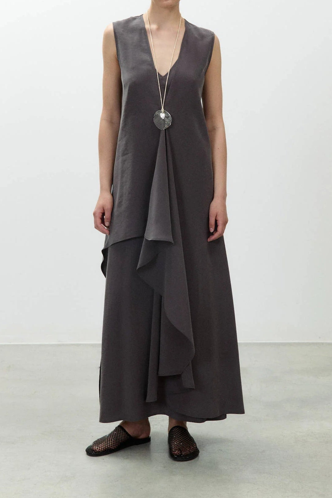 Woman wearing a sleeveless gray dress with a layered design on a white background