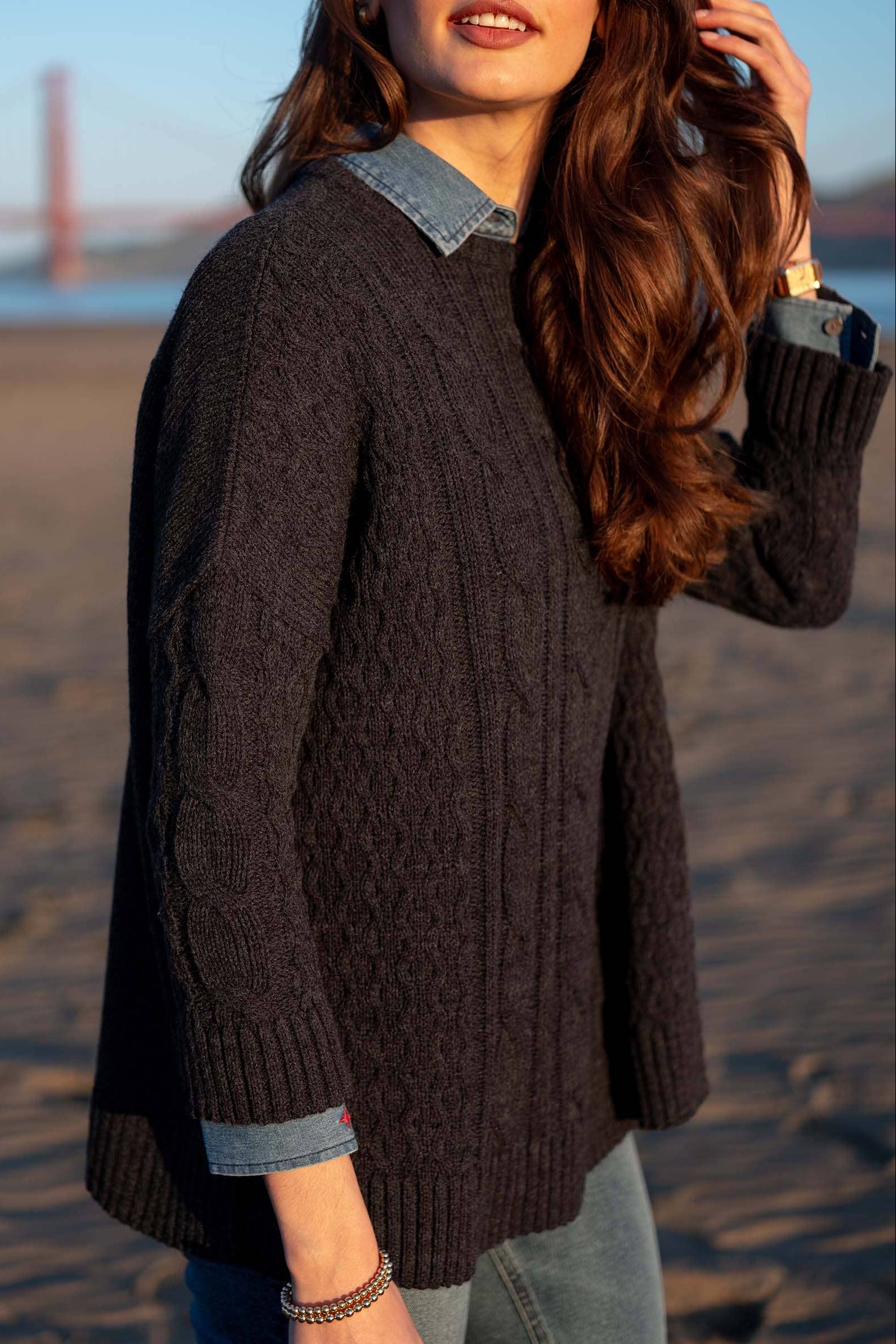 Woman wearing a dark brown sweater on a beach with a blurred background