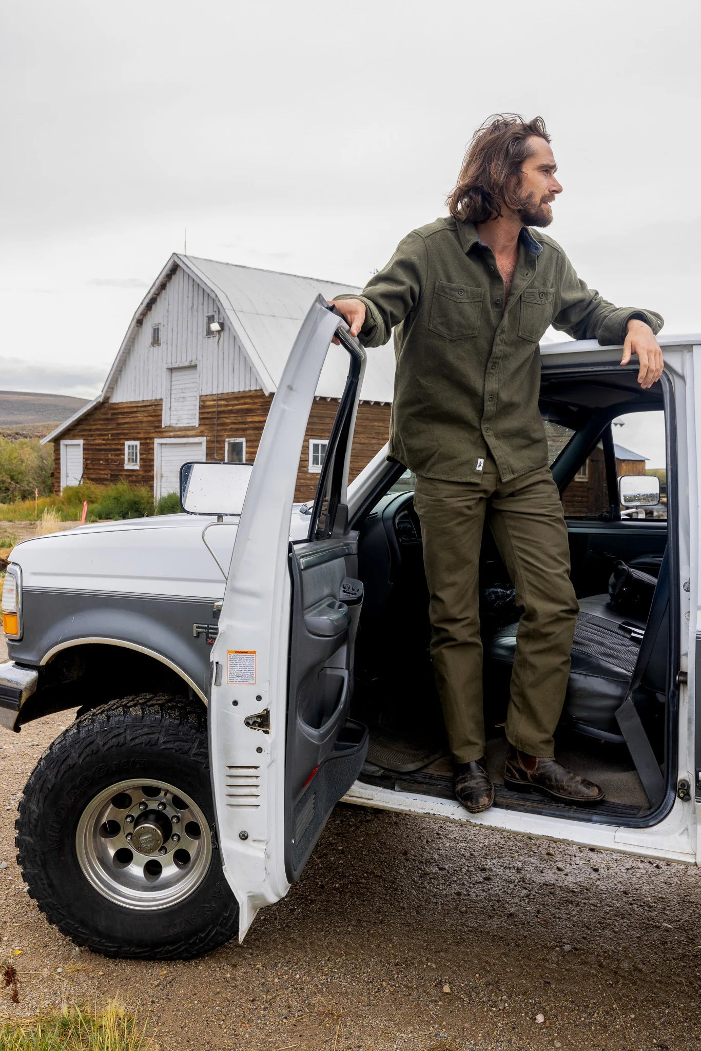 Man standing next to an open truck door in a rural setting with a barn in the background.