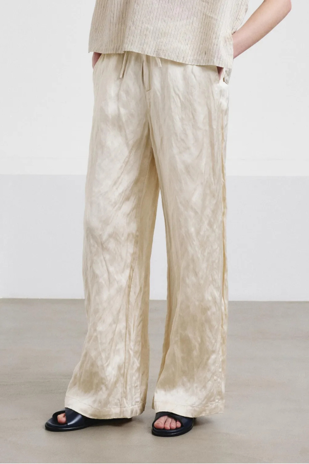 Woman wearing a beige outfit with wide-leg pants against a white background