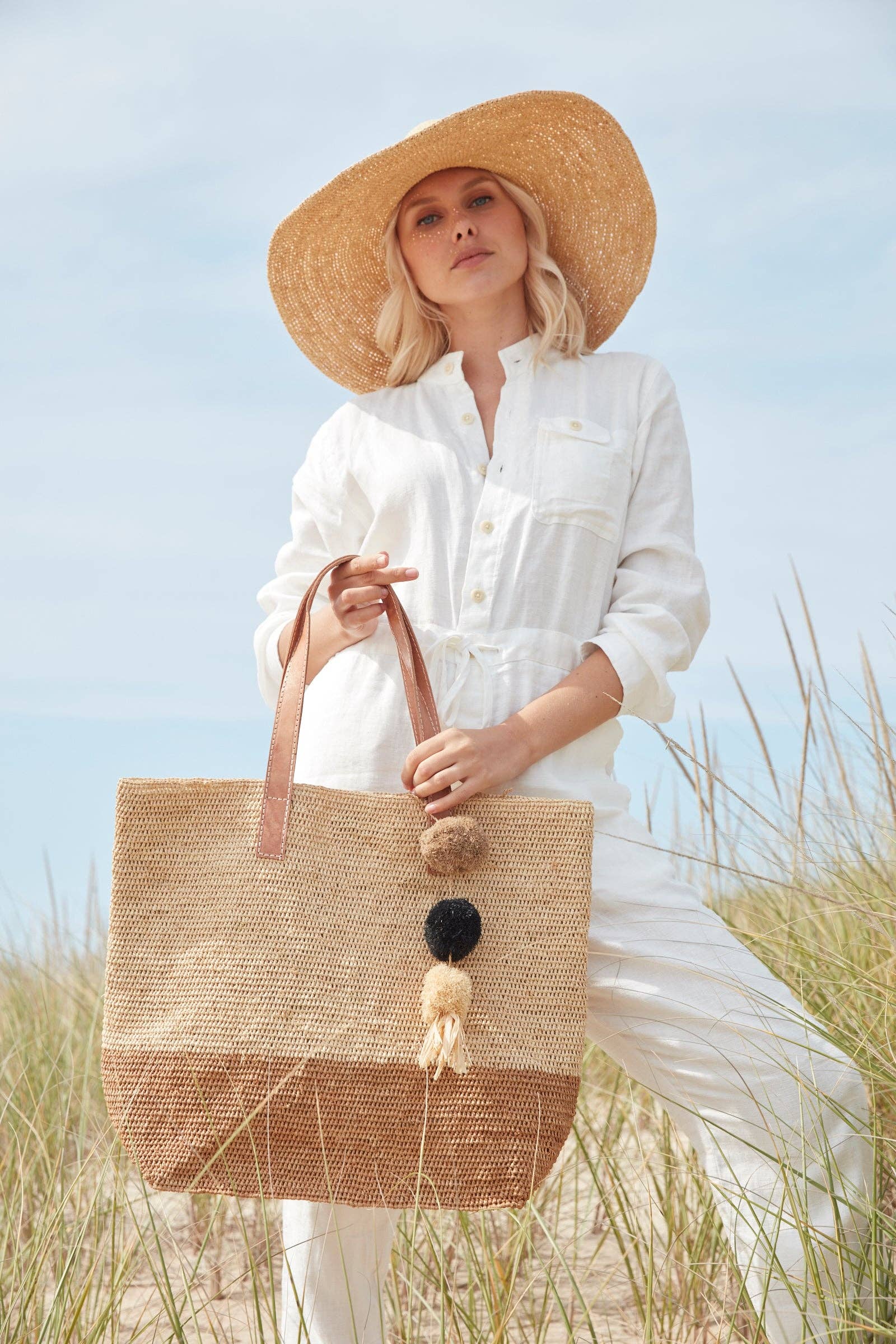 Woman holding a straw bag with pom-poms in a beach setting
