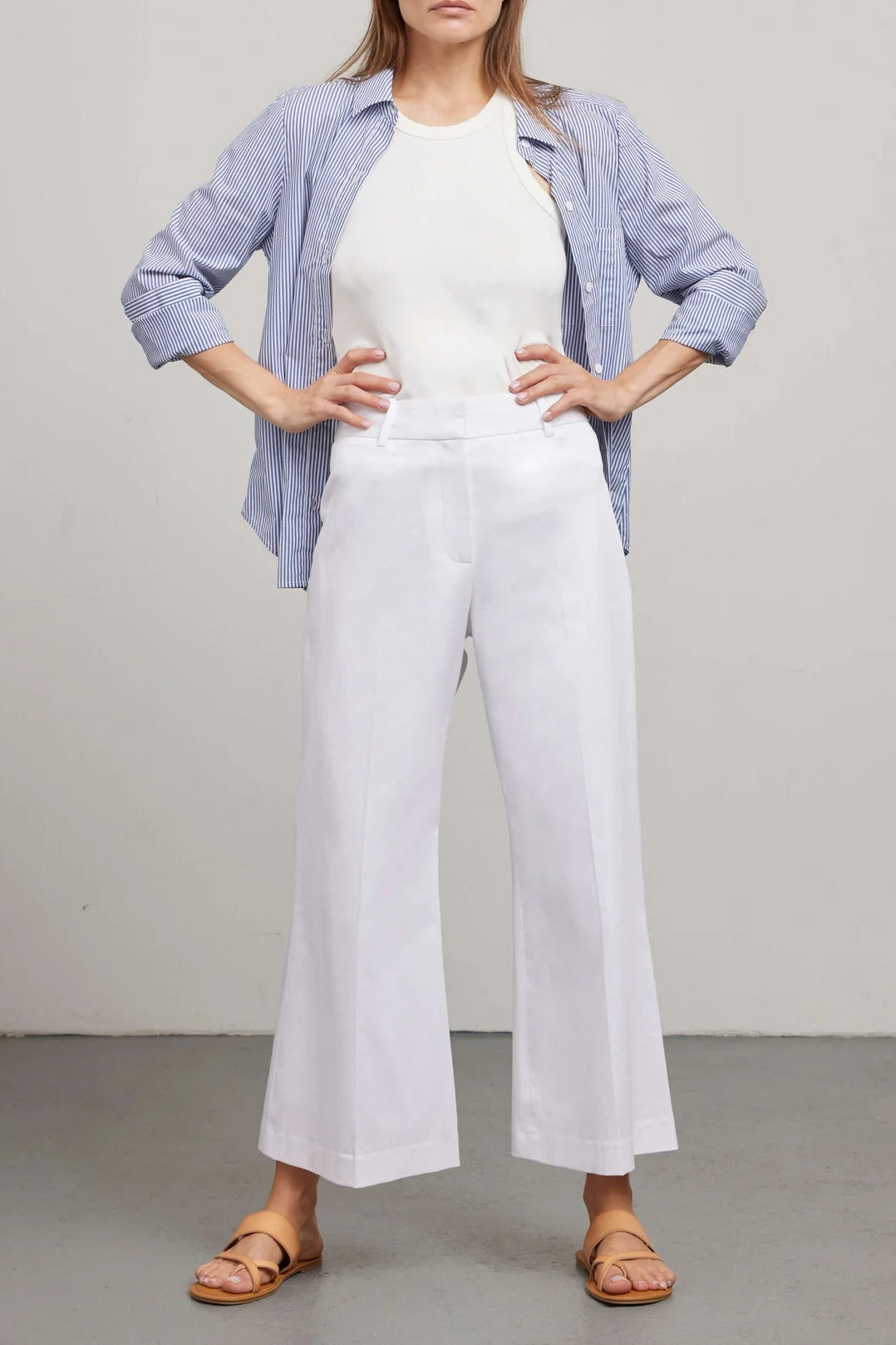 Woman wearing a blue checkered shirt, white top, and white wide-leg pants against a plain background.