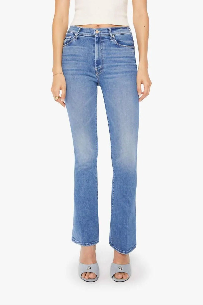 A model wearing light-wash blue flare jeans, a white ribbed tank top, and gray heeled sandals, standing against a plain white studio background.