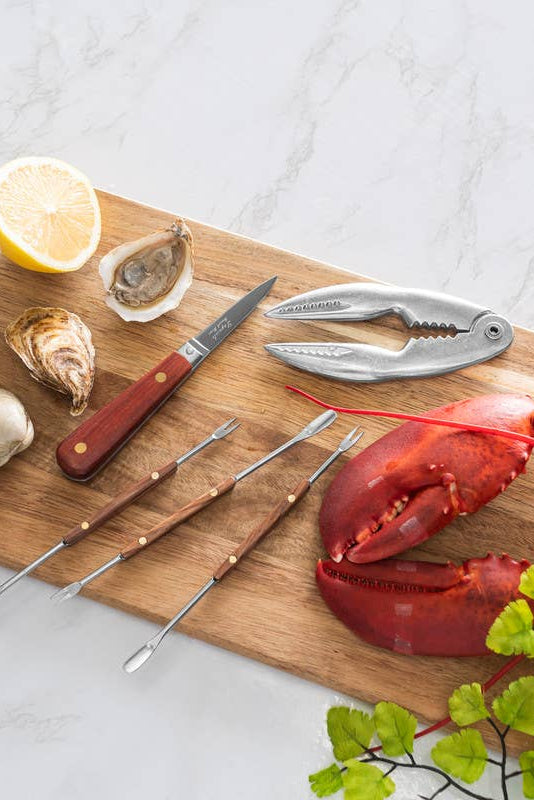 Wooden cutting board with seafood tools, lobsters, and oysters on a white surface.