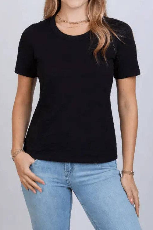 Woman wearing a black t-shirt and light blue jeans against a plain background