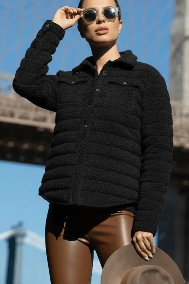Person wearing a black puffer jacket with sunglasses and a hat on a bridge background