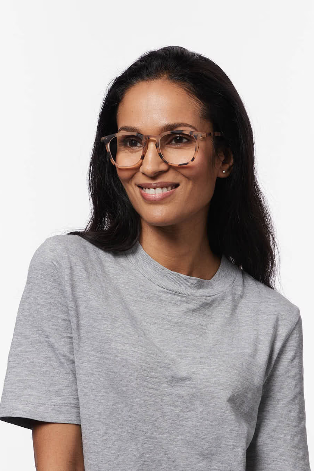 A woman with long dark hair wearing tortoiseshell square eyeglasses and a light gray crewneck t-shirt, photographed against a plain white background.