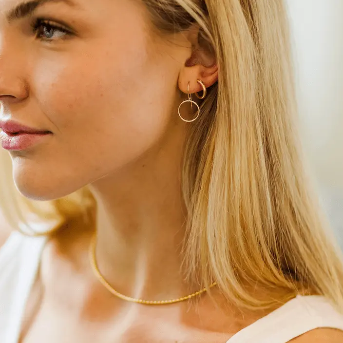 Close-up of a woman wearing gold hoop earrings and a necklace.