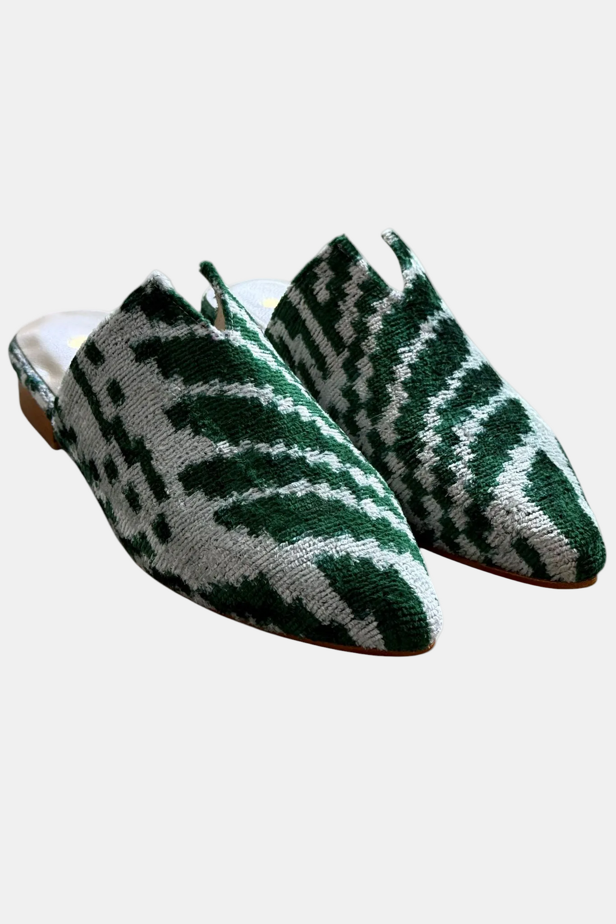 A pair of pointed-toe mule slippers featuring a green and white woven ikat pattern, shown against a plain white background.