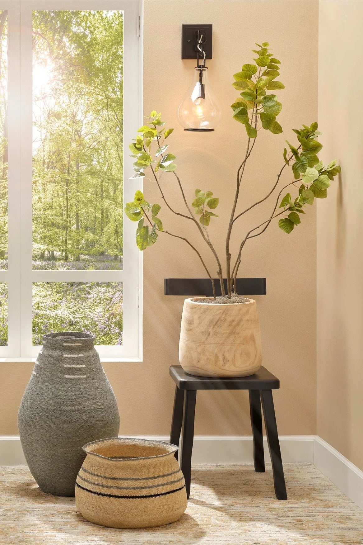 Decorative vases and a plant in a room with a window view of greenery.