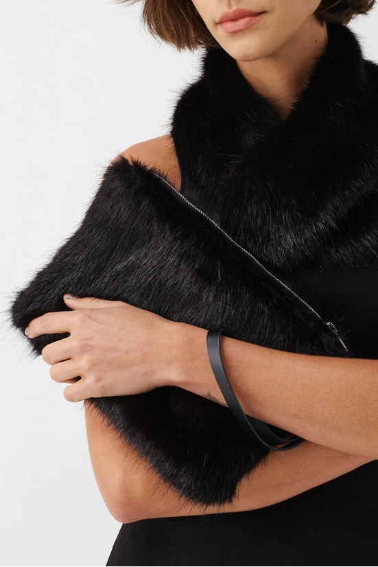 A woman modeling a black faux fur cowl neck warmer and matching black clutch bag against a light gray studio background.