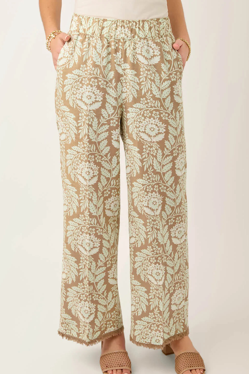A person wearing loose, wide-leg pants with an allover floral print in beige and off-white, paired with tan heeled sandals against a plain light background.
