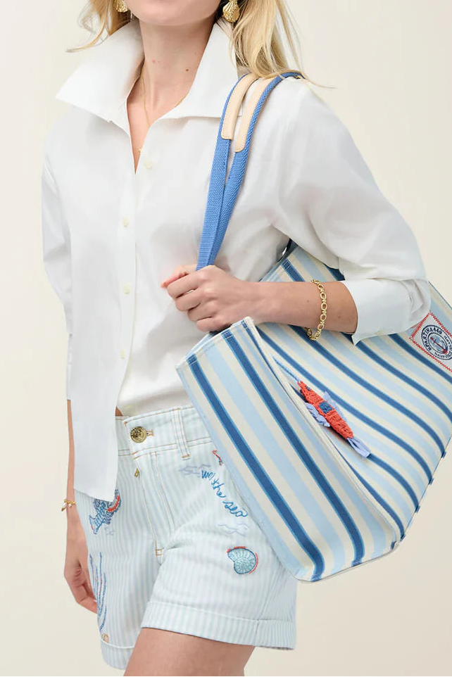 Woman holding a blue and white striped tote bag against a plain background