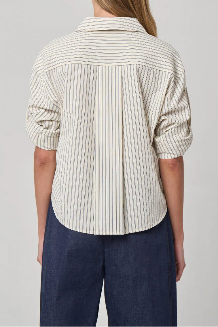 Person wearing a striped shirt and dark pants on a plain background