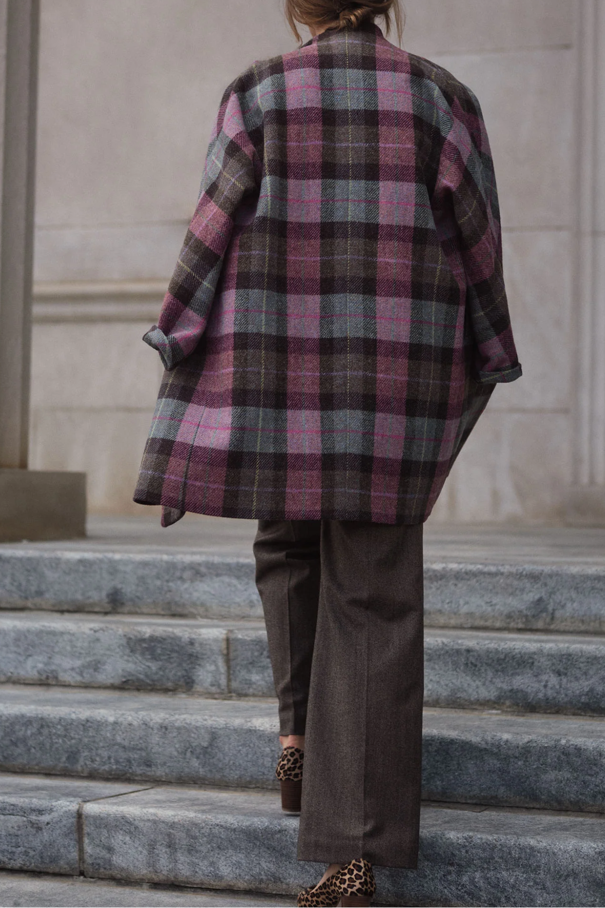 Person wearing a plaid coat and brown pants standing on stone steps.