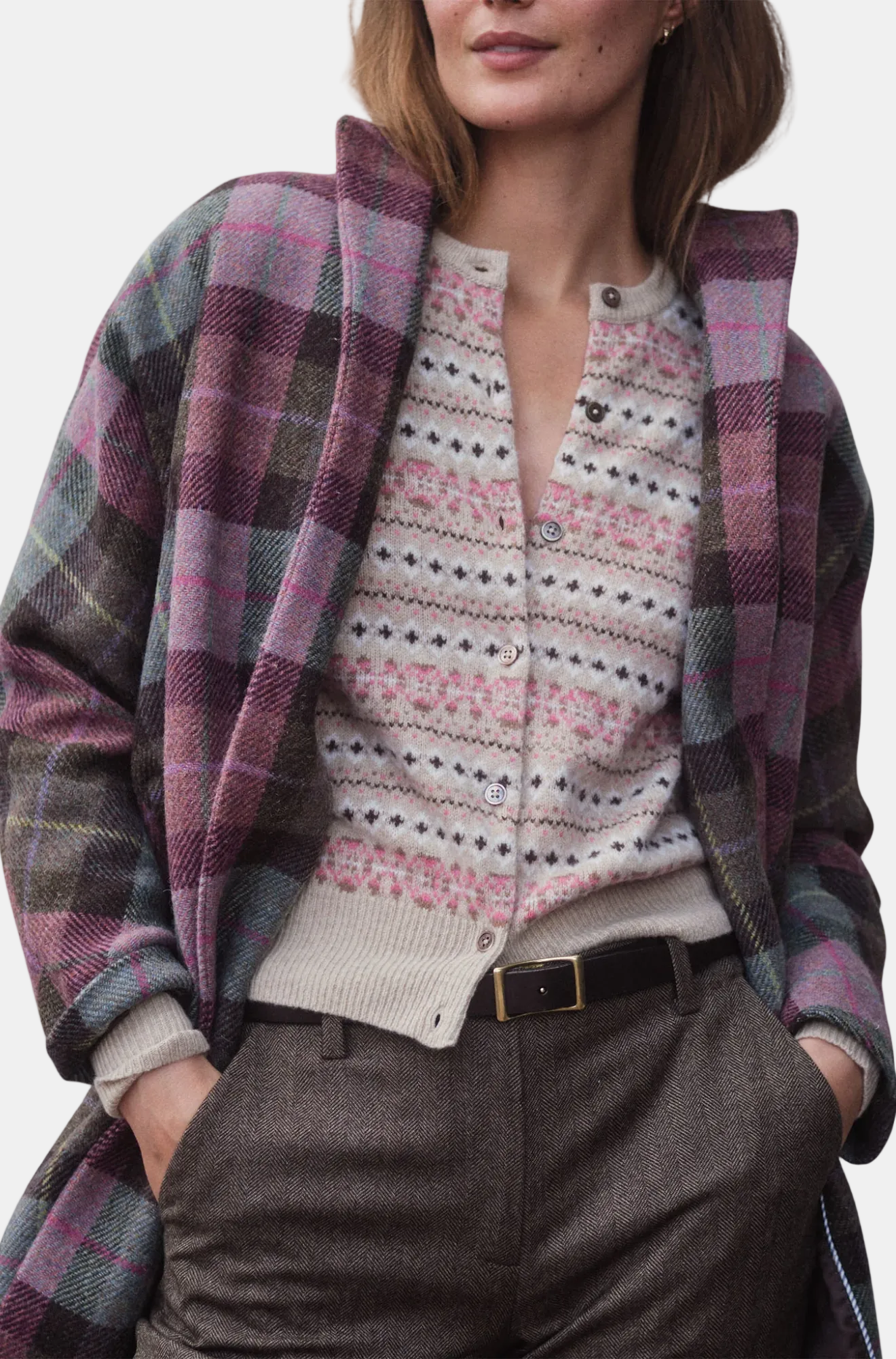 Person wearing a plaid shirt over a patterned sweater with a white background