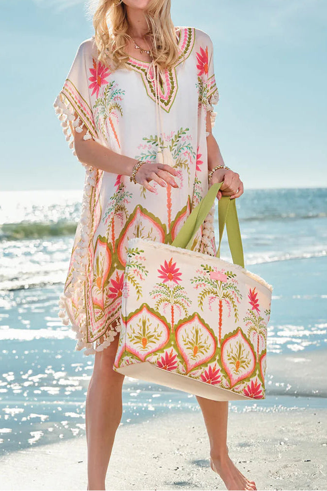 Woman in a colorful dress holding a matching tote bag on a beach.