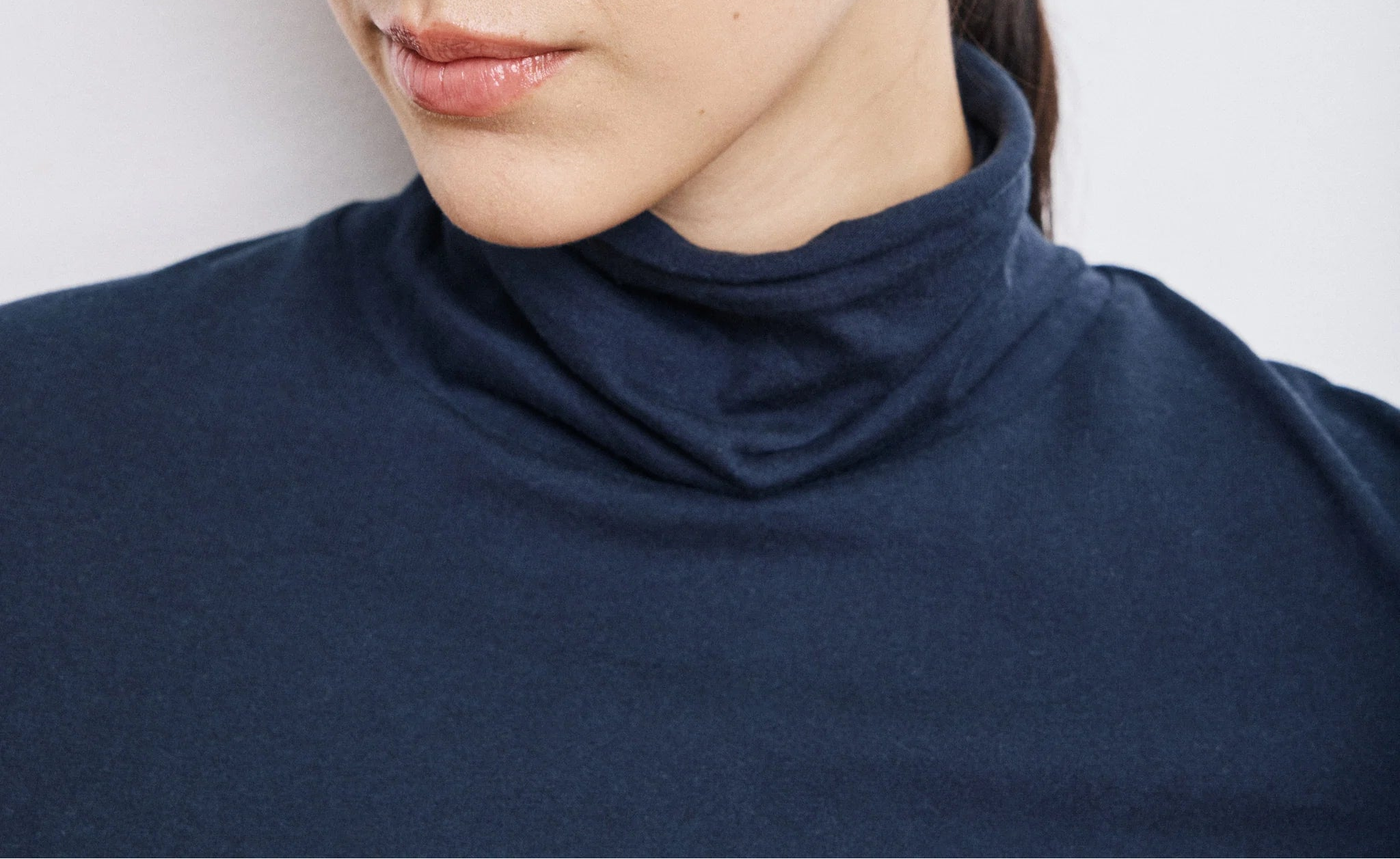 Close-up of a person wearing a navy turtleneck and gold earring against a white background