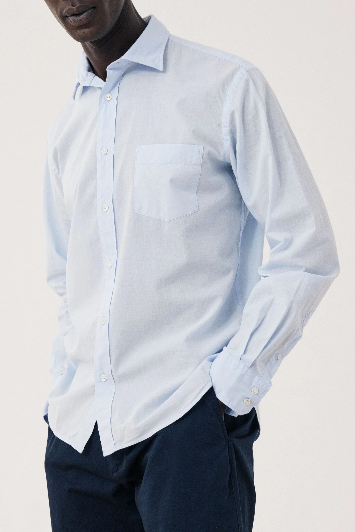 Man wearing a light blue shirt and dark pants against a plain background
