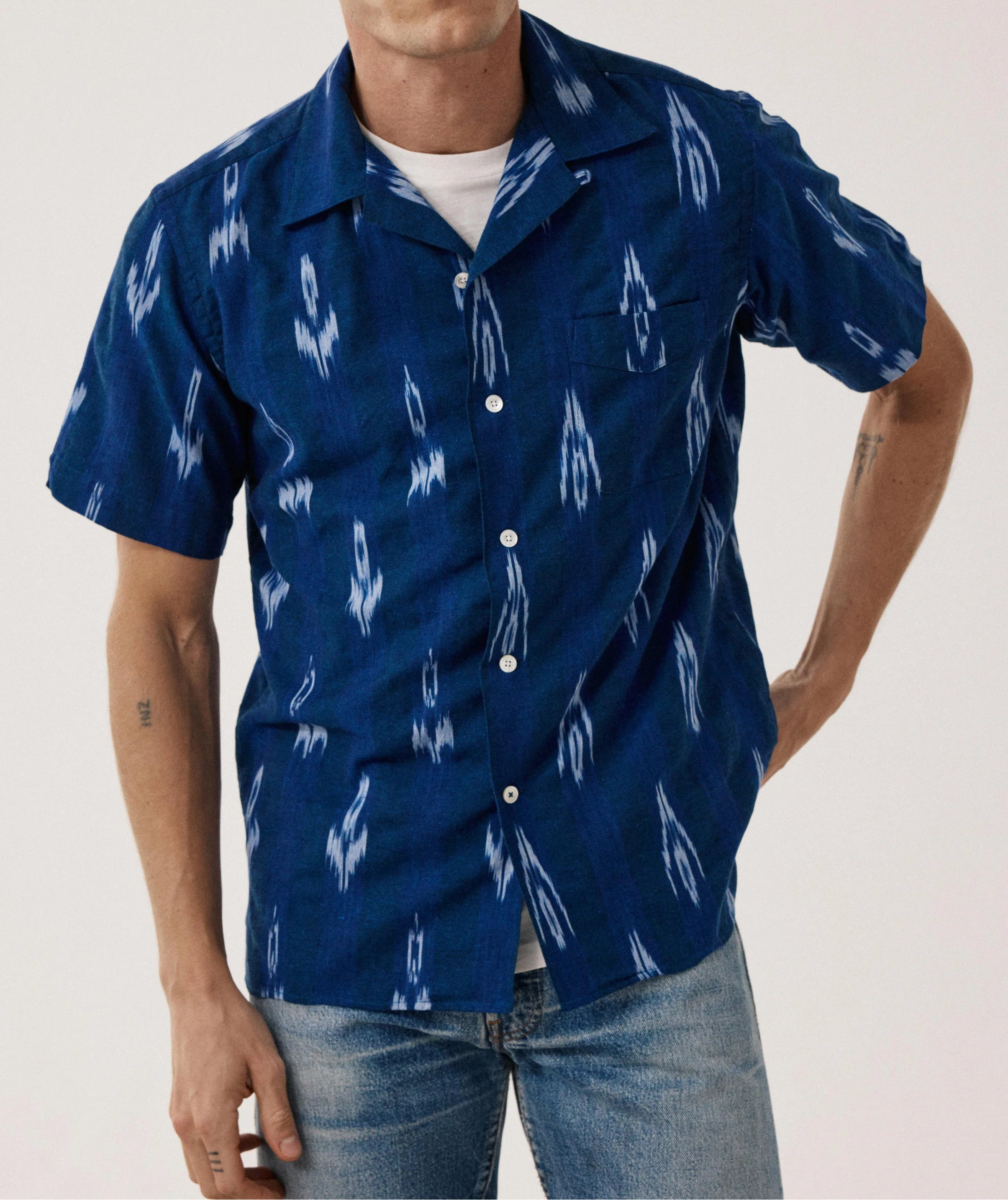 Man wearing a blue patterned shirt and jeans on a white background