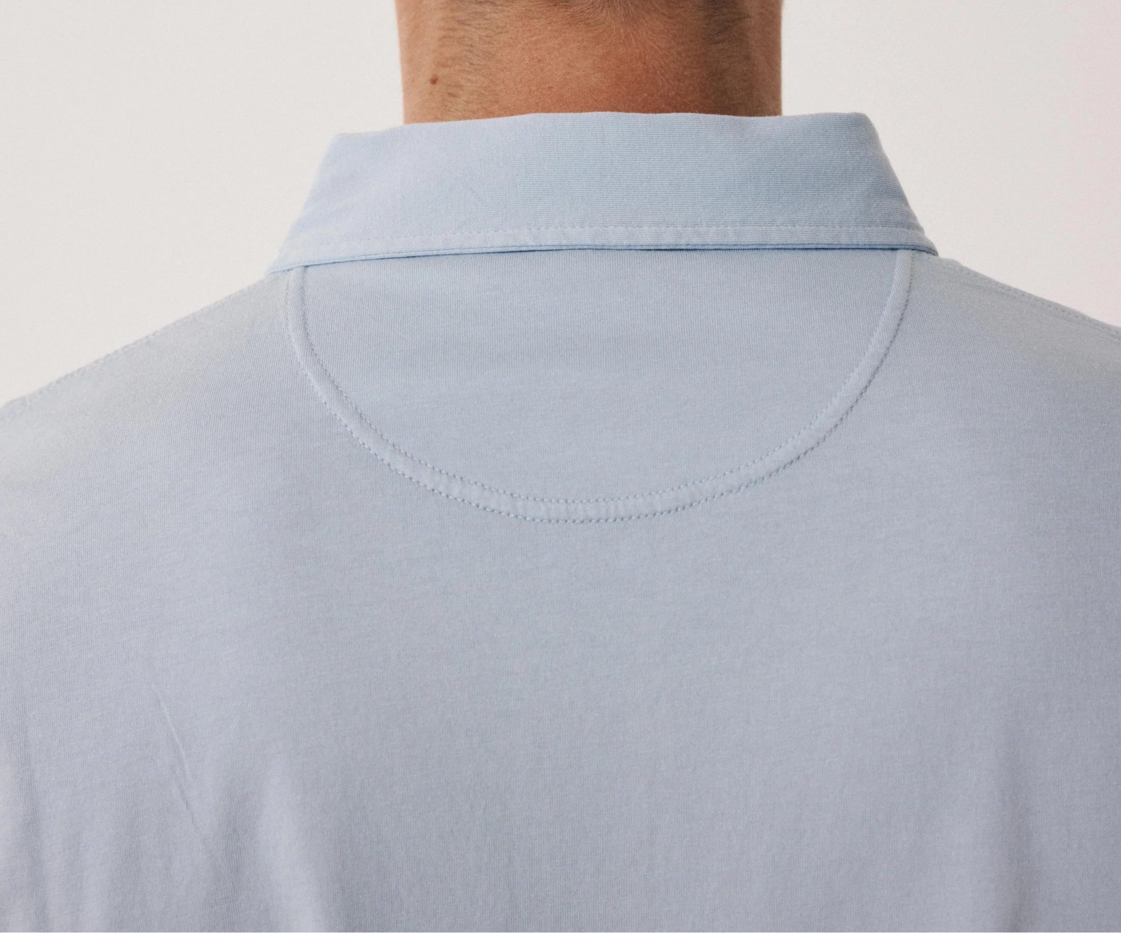 Back view of a person wearing a light blue shirt against a plain background
