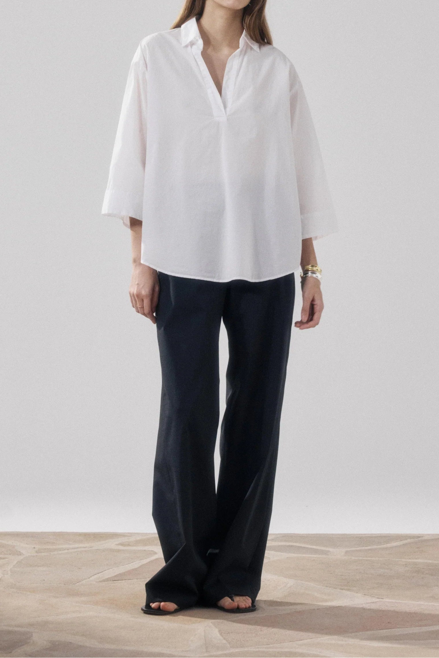Woman wearing a white blouse and black pants on a plain background
