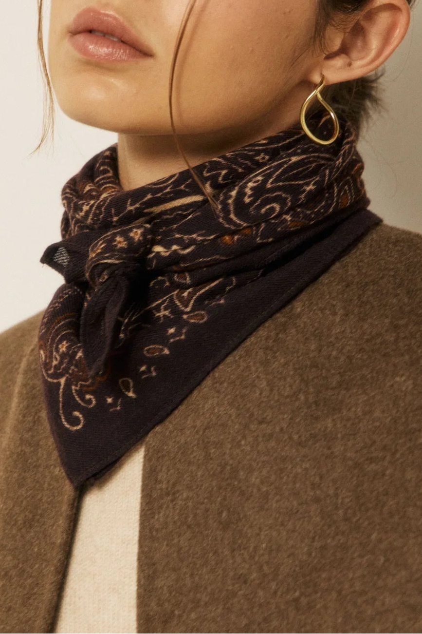A close-up of a woman wearing a dark brown and black paisley patterned neck scarf tied under her collar, paired with a brown wool vest over a cream sweater.
