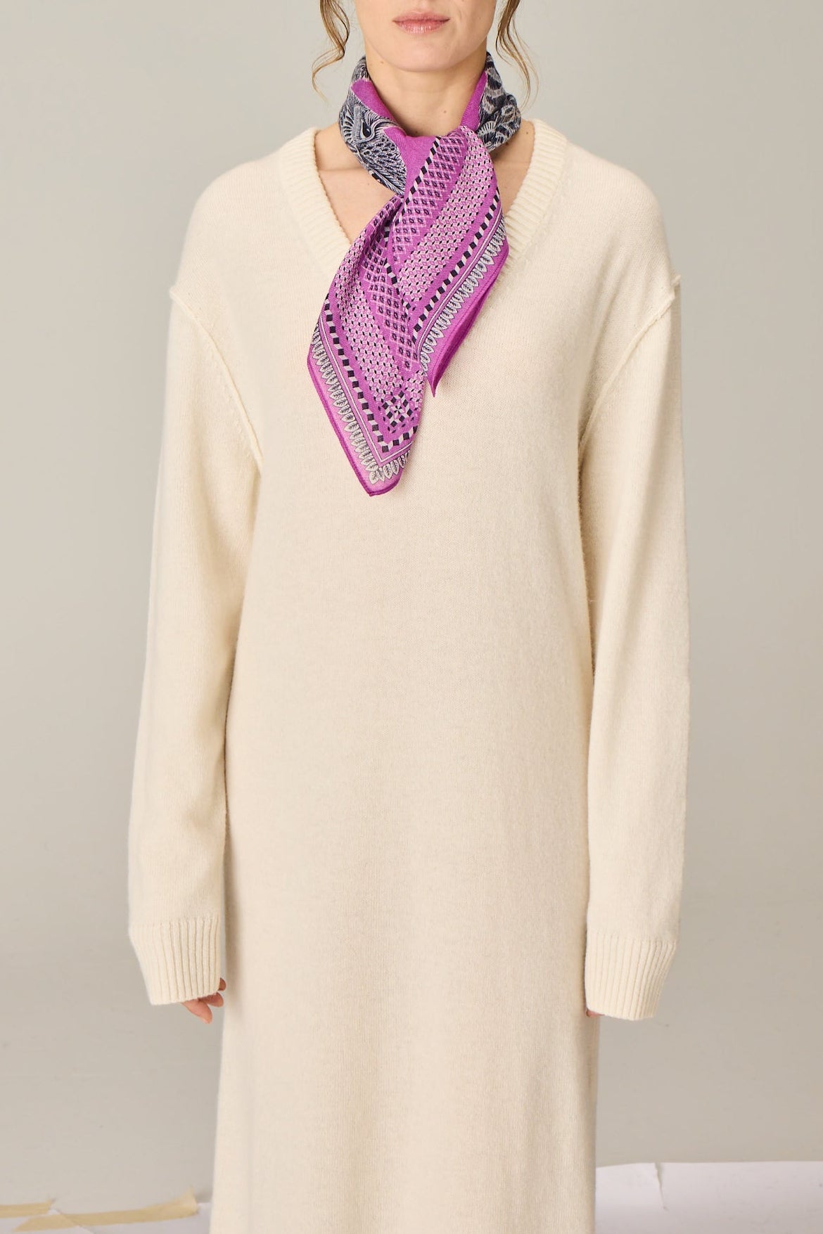 Woman wearing a beige dress and colorful scarf against a plain background