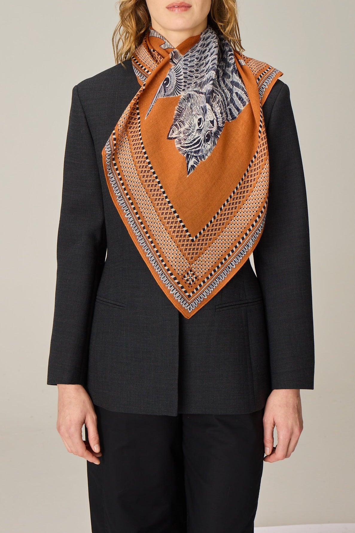 Woman wearing a black blazer and patterned orange scarf against a plain background