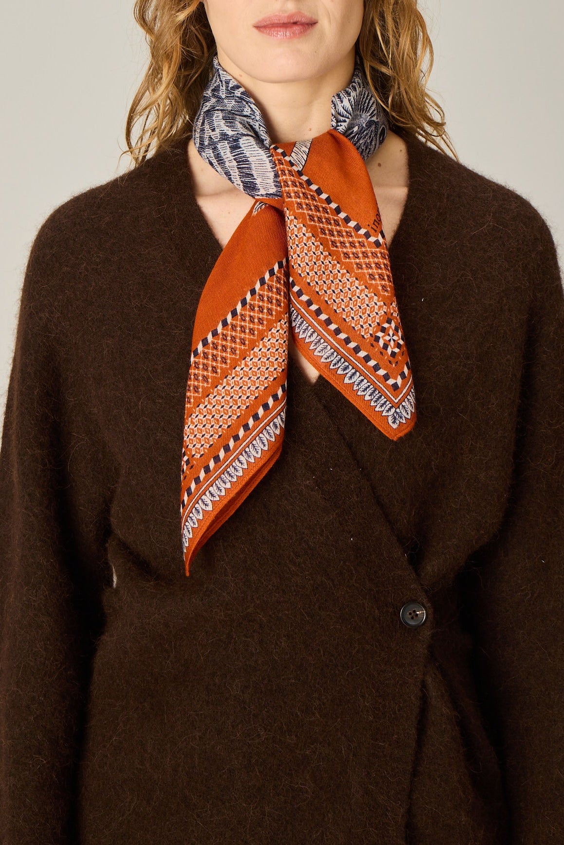 Woman wearing a brown coat and patterned scarves on a plain background