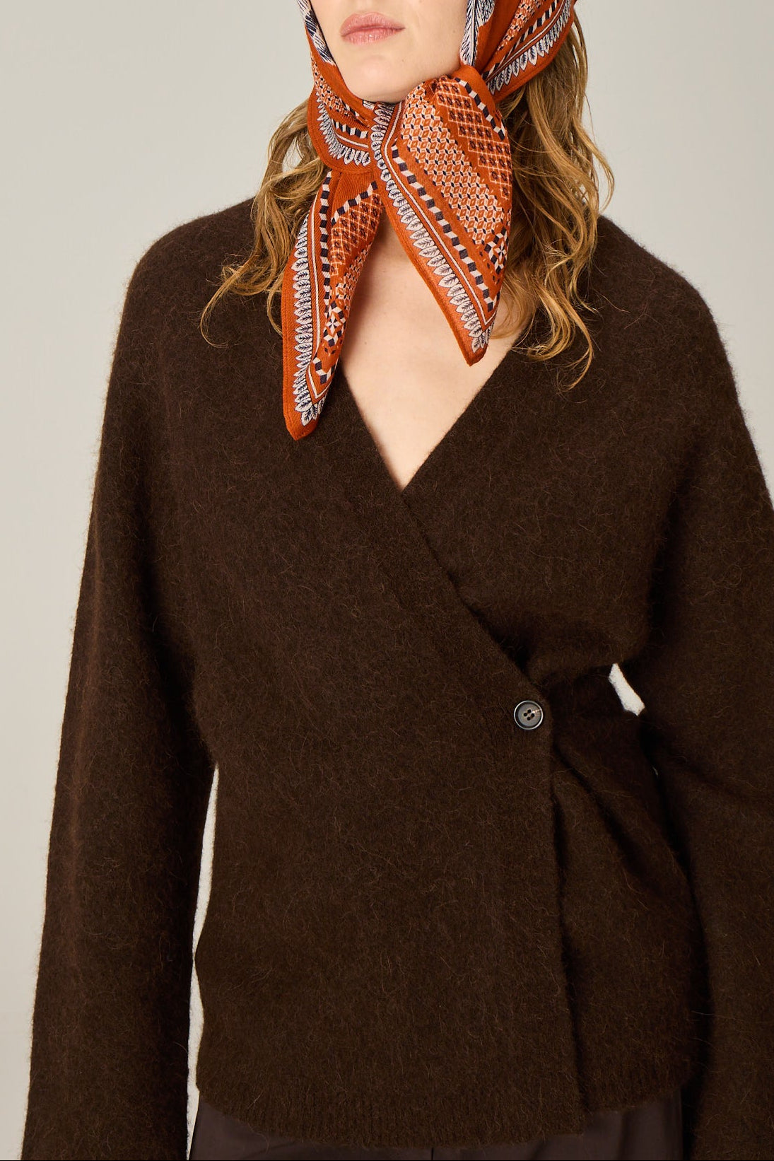 Woman wearing a brown jacket and an orange patterned scarf on a plain background