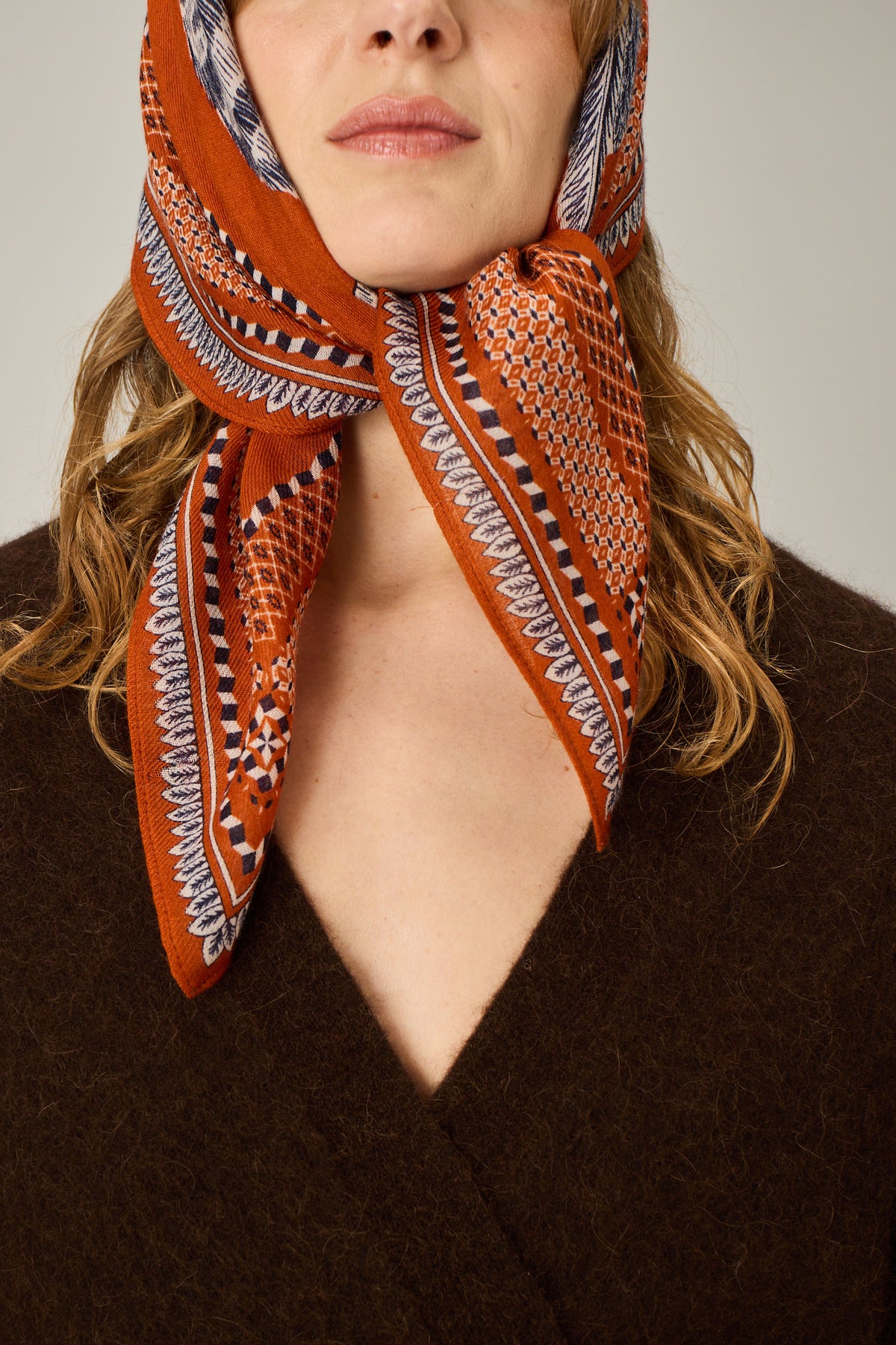 Person wearing a patterned orange scarf on a neutral background
