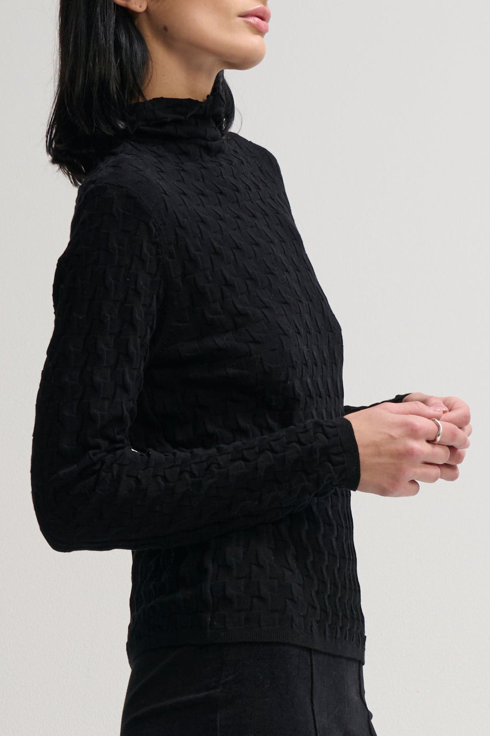 Woman wearing a black cable knit sweater against a plain background