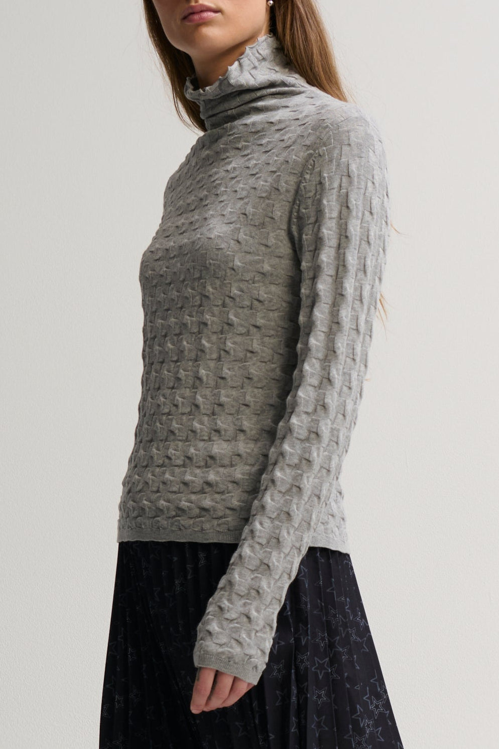 Woman wearing a gray turtleneck sweater against a plain background