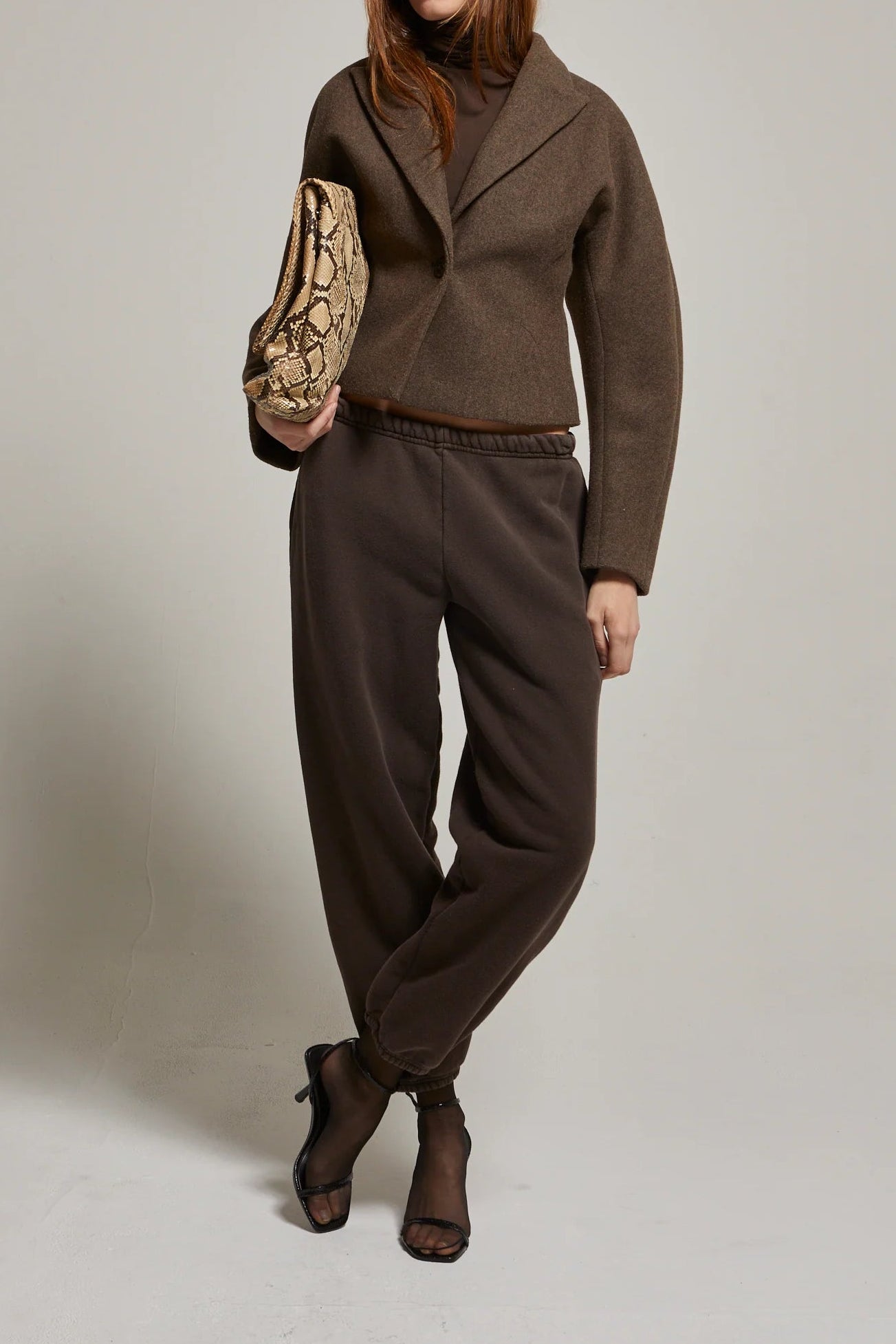 Person wearing a brown outfit with a patterned bag on a plain background